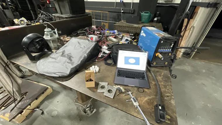 A cluttered workbench with a laptop, a helmet, and hand tools.