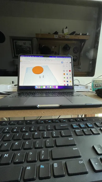 A laptop on a desk showing the same circular part in CAD.