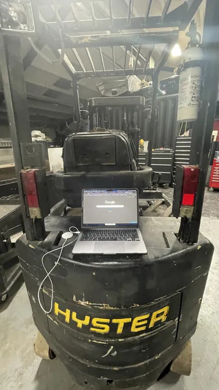 A laptop balanced on the counterweight of a forklift in the workshop.