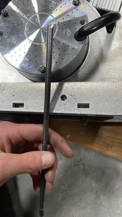 A hand holding a steel rod in front of a lathe faceplate.
