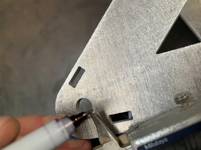 A hand marking cut lines on a sheet of aluminum with a pen.