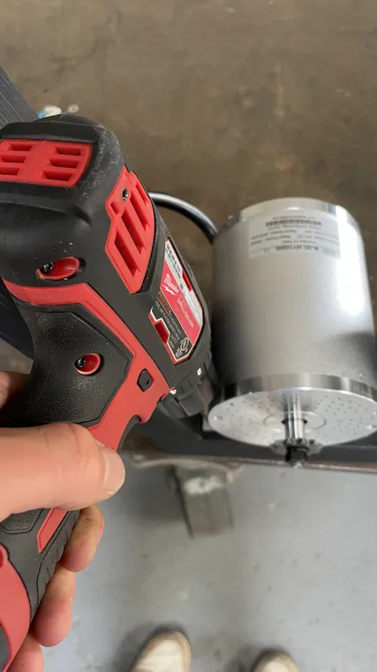 A hand holding a drill against the end of the motor housing.
