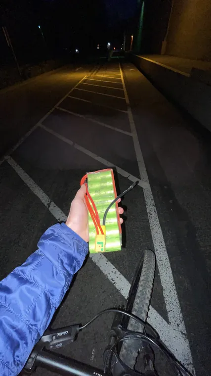 A hand holding a green battery pack over a road at night.