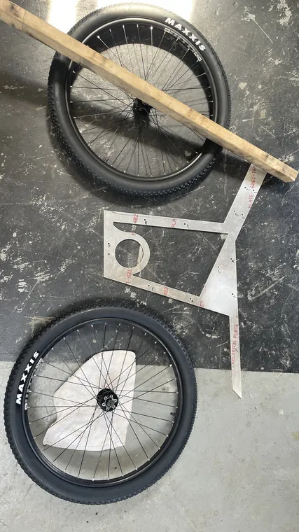 Two bicycle wheels laid out on the floor beside the wooden frame parts.