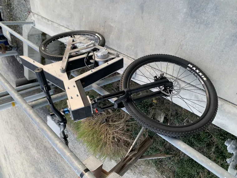 The wooden-framed bike leaning against a rail outdoors.