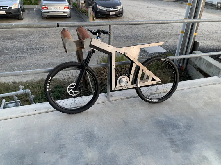 The wooden-framed bike standing complete against a fence outdoors.
