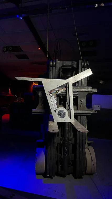 The bare aluminum frame hanging from the forklift under blue light.