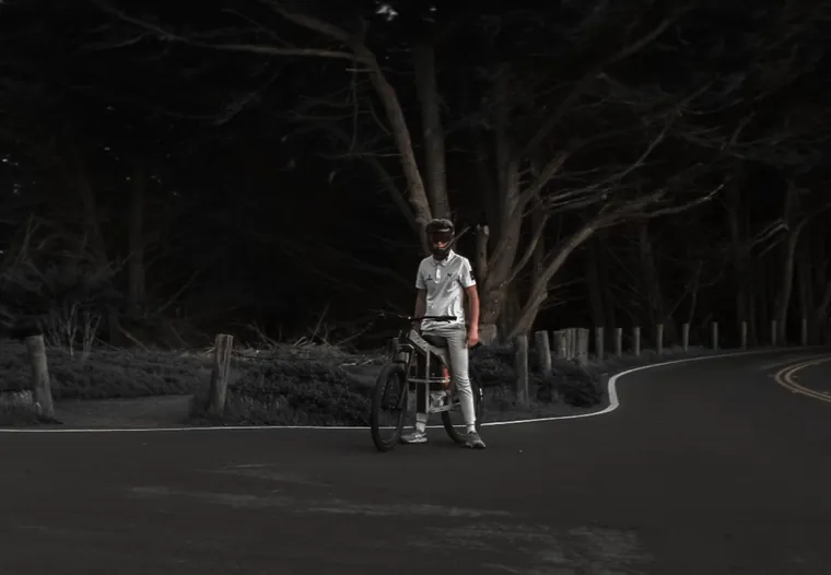 A rider standing beside The Nacho on a dark tree-lined road at night.