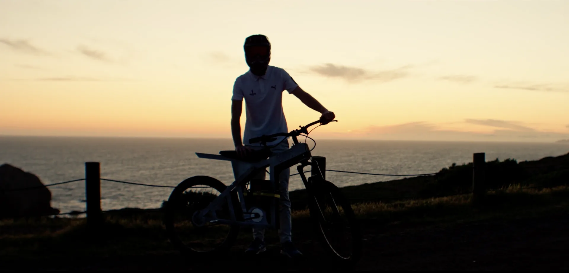 A rider standing over The Nacho in silhouette against an orange sunset over the ocean.