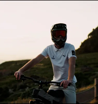 A rider in a helmet and goggles sitting on The Nacho on a coastal hillside.